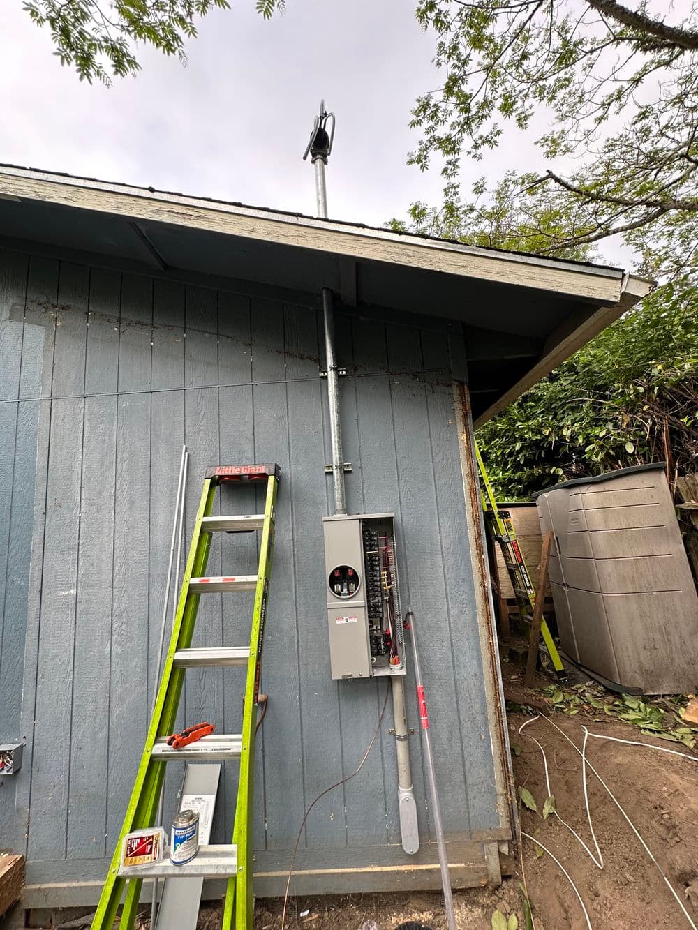 Electrical panel installation on a blue house exterior with a ladder nearby.