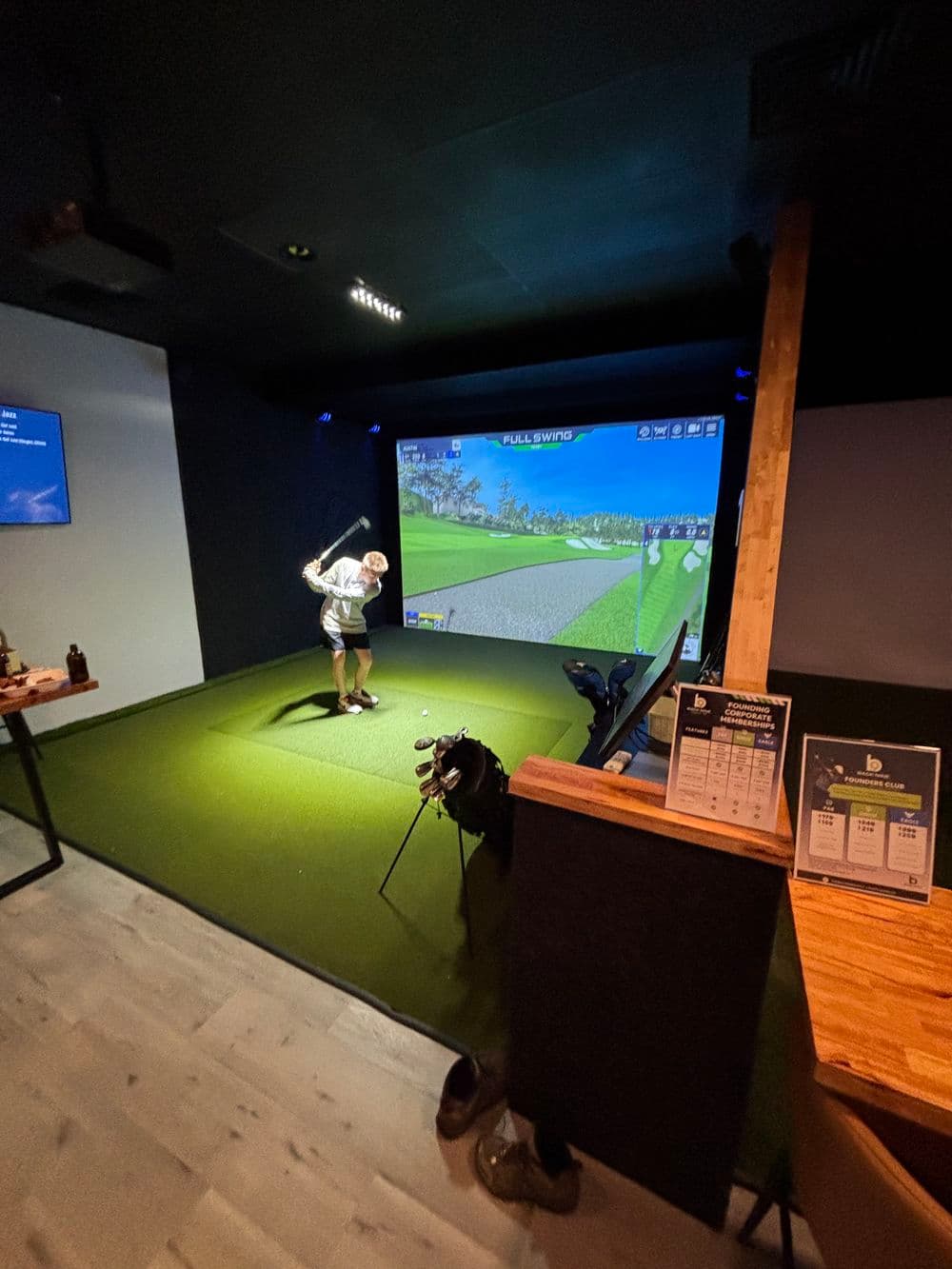 Indoor golf simulator with player swinging club, realistic virtual course displayed on screen.