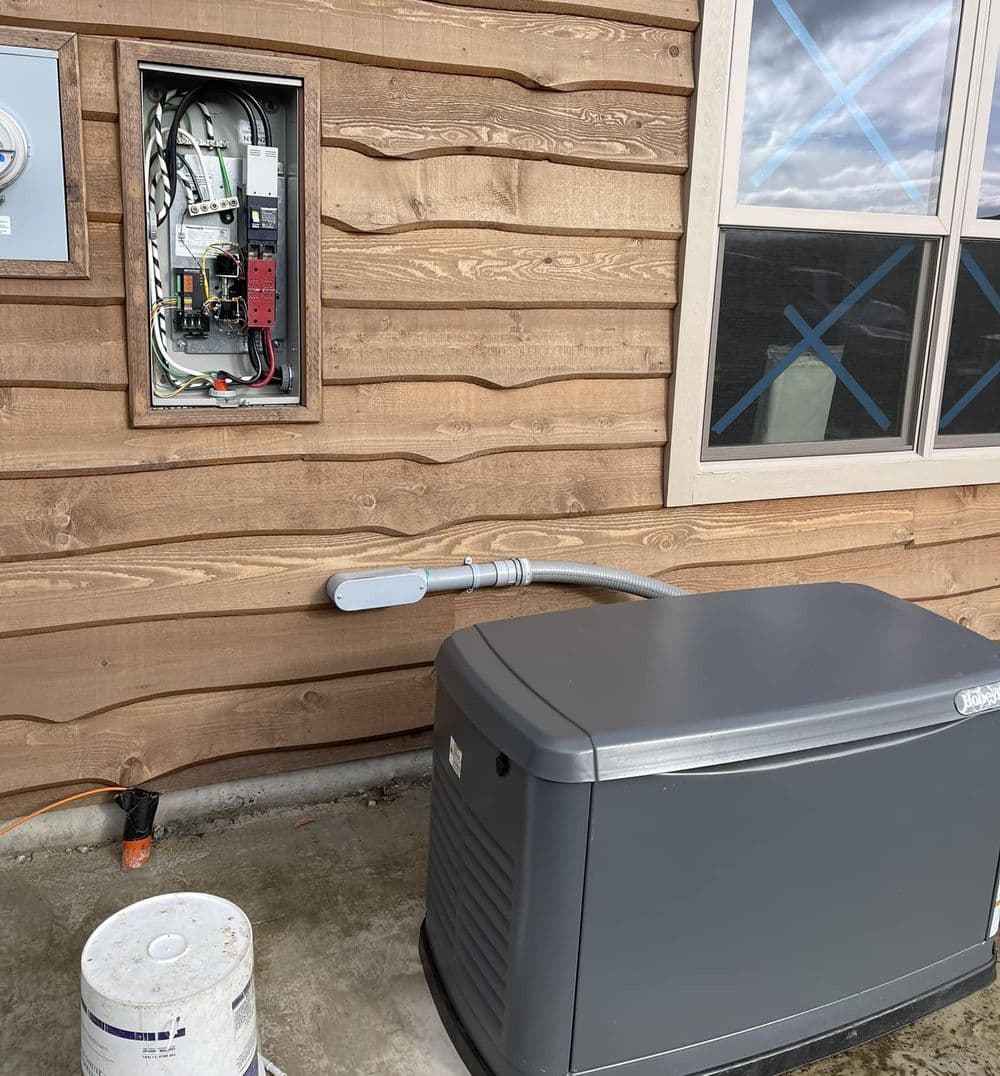 Generator installation beside electrical panel on wooden exterior wall.